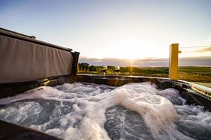Bubbling hot tub on a deck overlooking a scenic landscape at sunset.