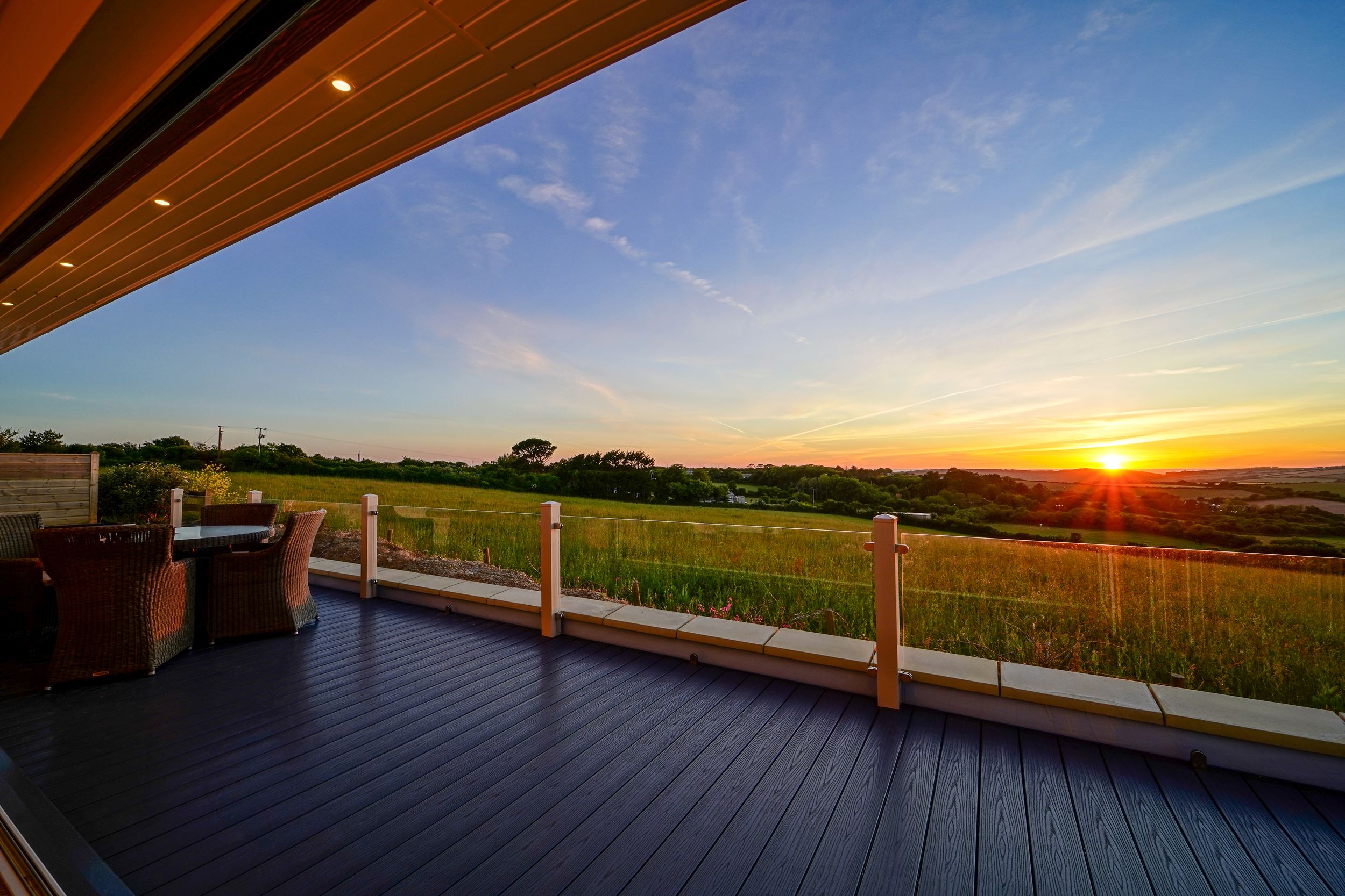 Wooden deck with railing overlooking scenic rural farmland during a vibrant orange sunset.