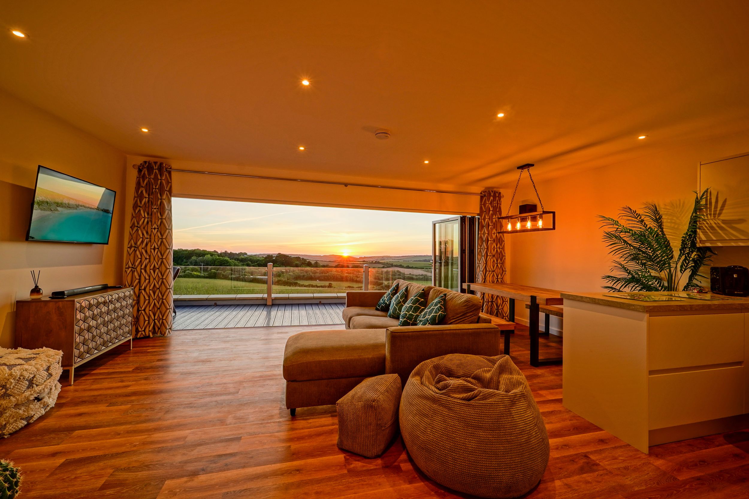 Spacious living area with orange sunset glow through windows and contemporary furnishings.