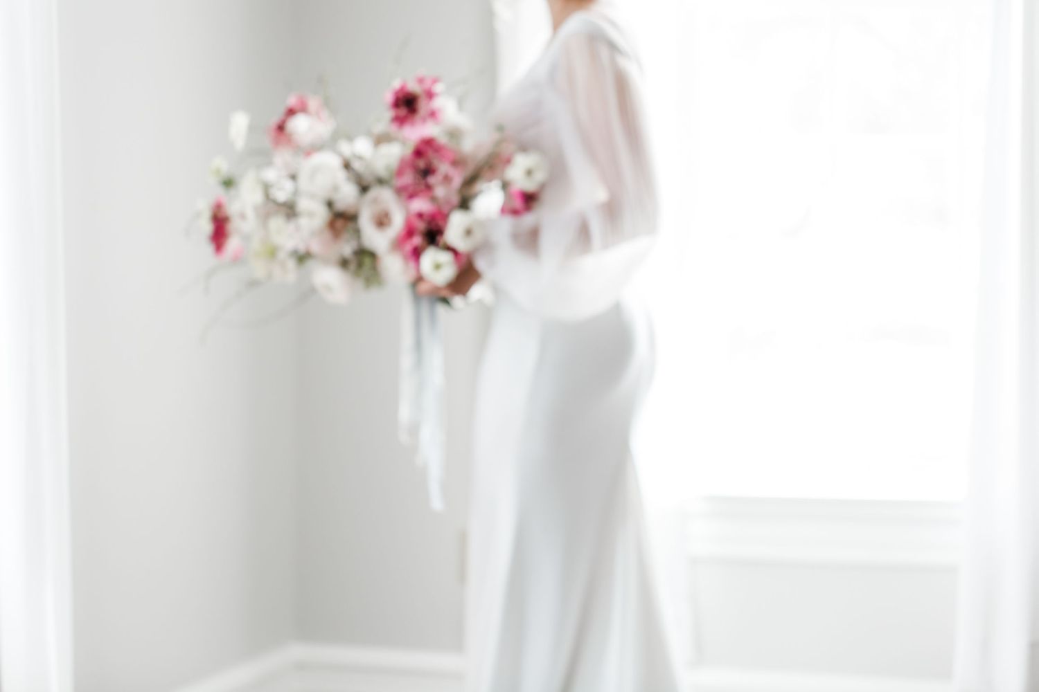 Elegant wedding dress with delicate pink and white floral bouquet in a bright indoor setting.