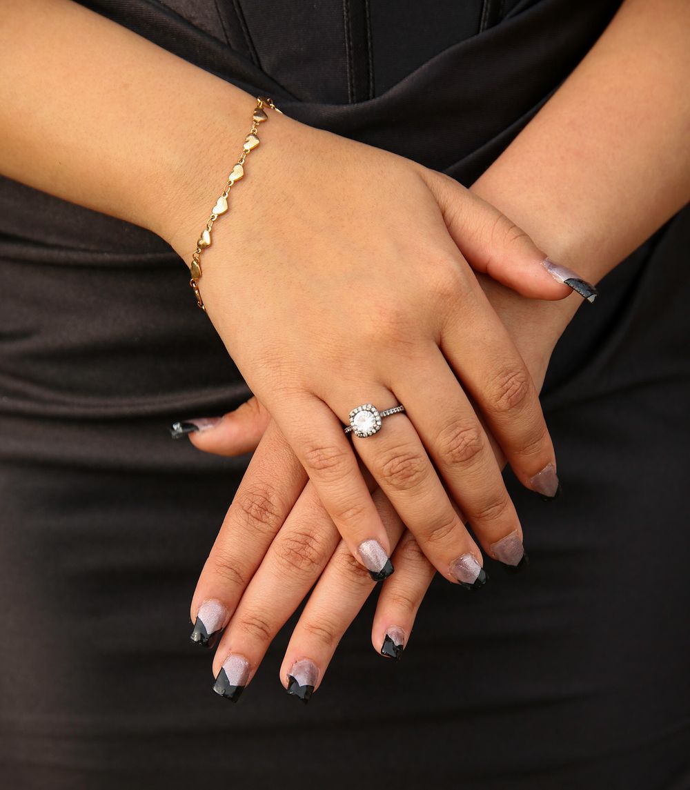 Hands wearing elegant gold jewelry display a delicate bracelet, sparkling ring and manicured nails with blue polish.