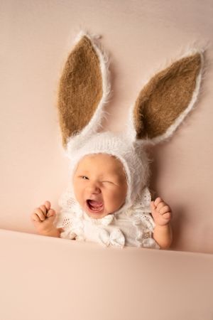Awake newborn baby on peach soft backdrop with bunny hat