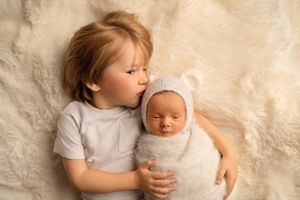 Newborn baby wrapped in white soft wrap with his older brother on beige fluffy rug