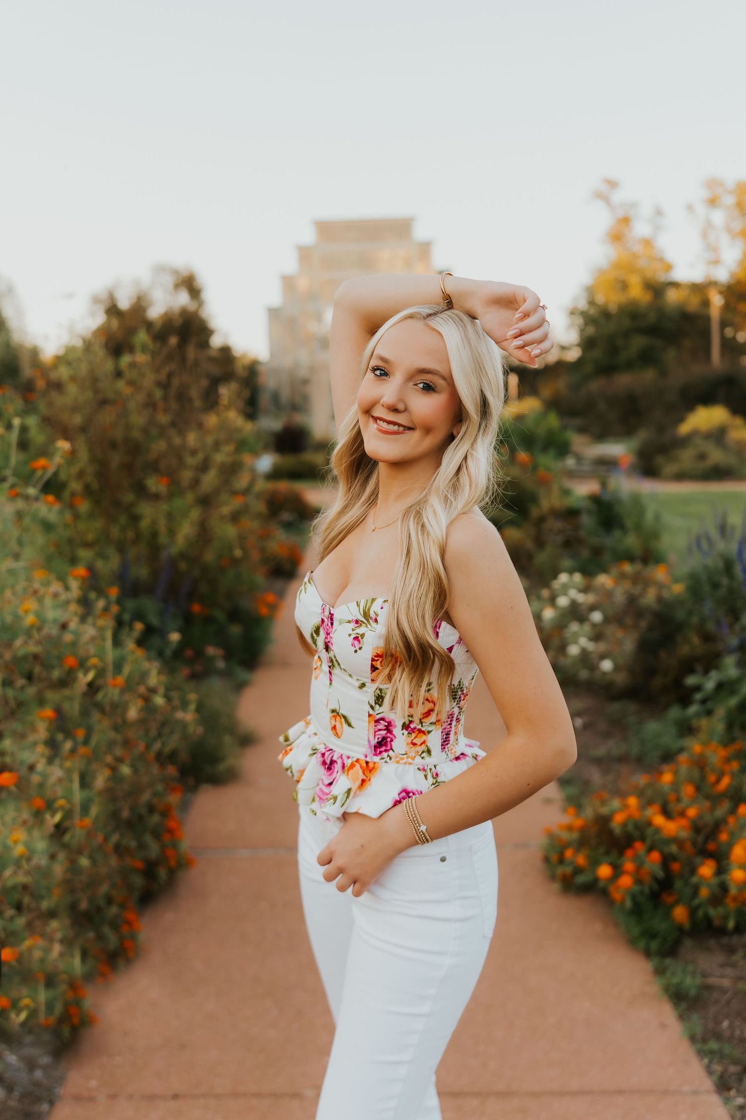 A blonde young woman wearing a brown dress is posing in front of a stone building with ivy.