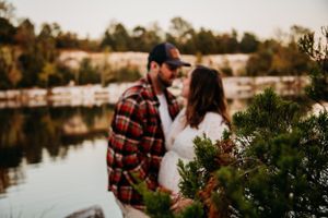 Couple sharing a kiss near a serene lake surrounded by lush greenery.