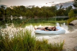 Woman relaxing on a white inflatable float on a calm scenic lake.