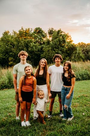 Group of six siblings posing together in a green field at sunset.