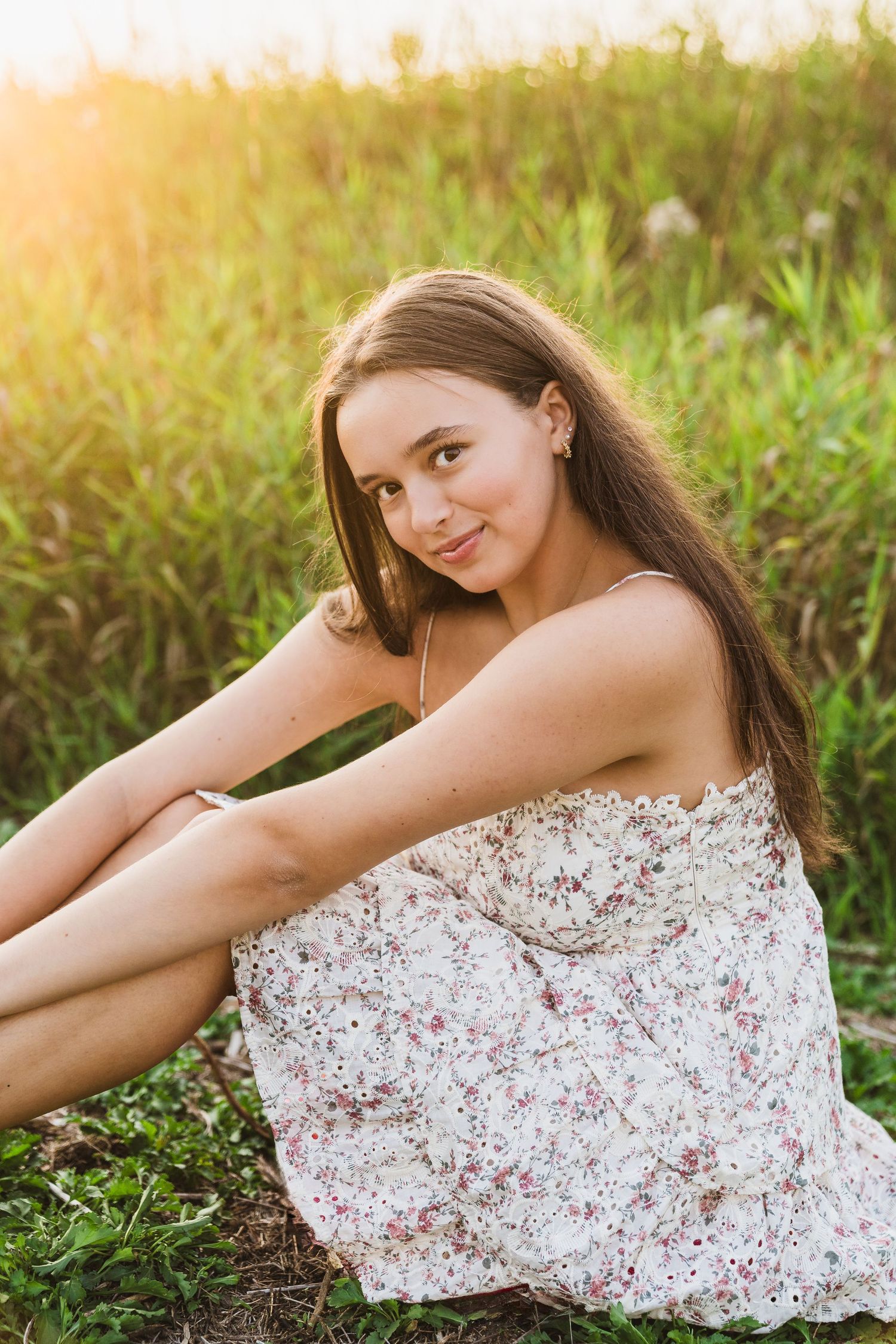 A graduate in black cap and gown poses joyfully in a field of wildflowers on a sunny day.