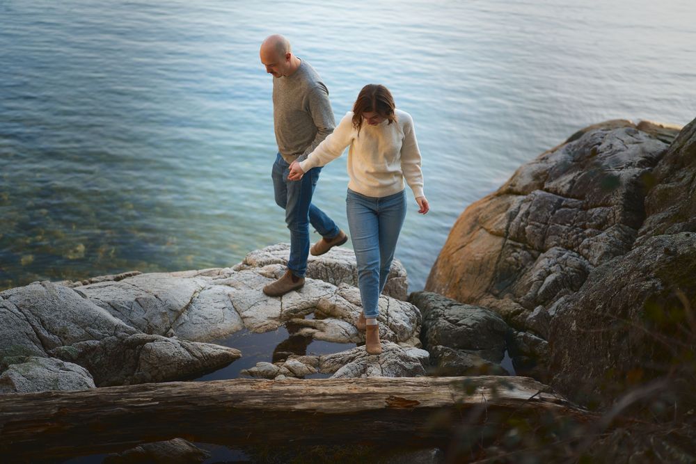 A couple walking along the rocks by the ocean, hand in hand.