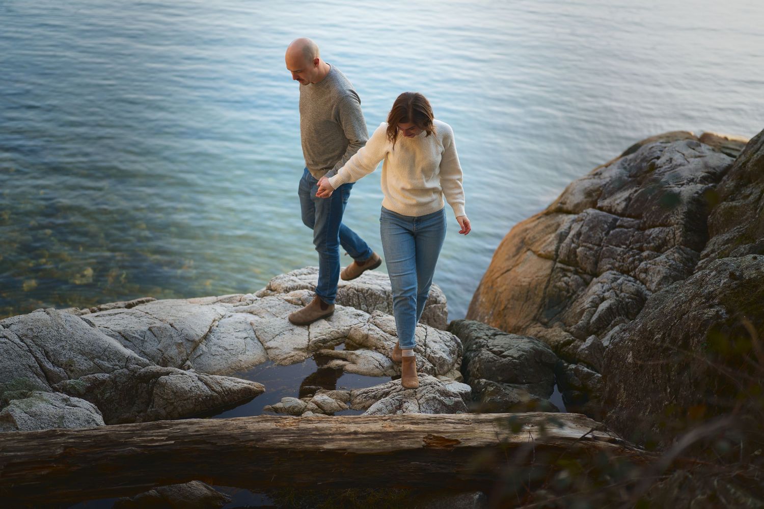 A couple walking along the rocks by the ocean, hand in hand.