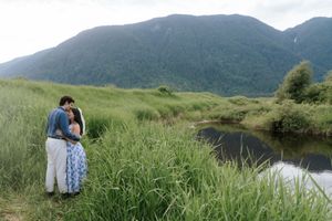 A couple embraces while standing beside a river with misty mountains in the background in Scotland.