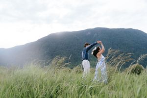 Couple enjoying a romantic moment in a misty mountainside meadow filled with tall green grass and wildflowers.