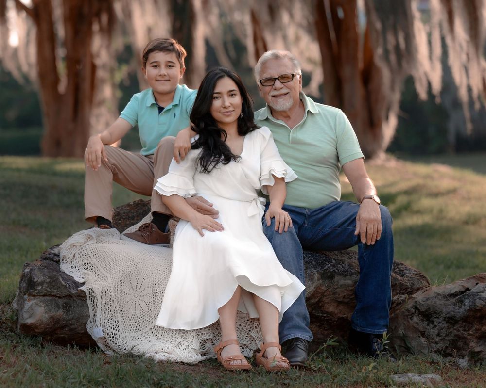 A family sits together on a large tree trunk in an outdoor setting wearing coordinated casual outfits.