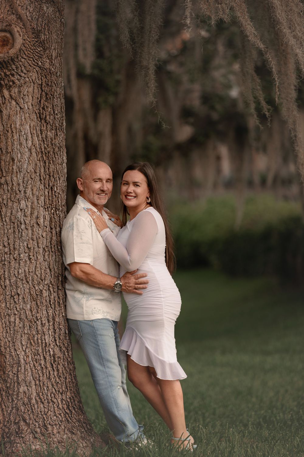 A couple shares intimate moments in a natural outdoor setting with trees in the background.