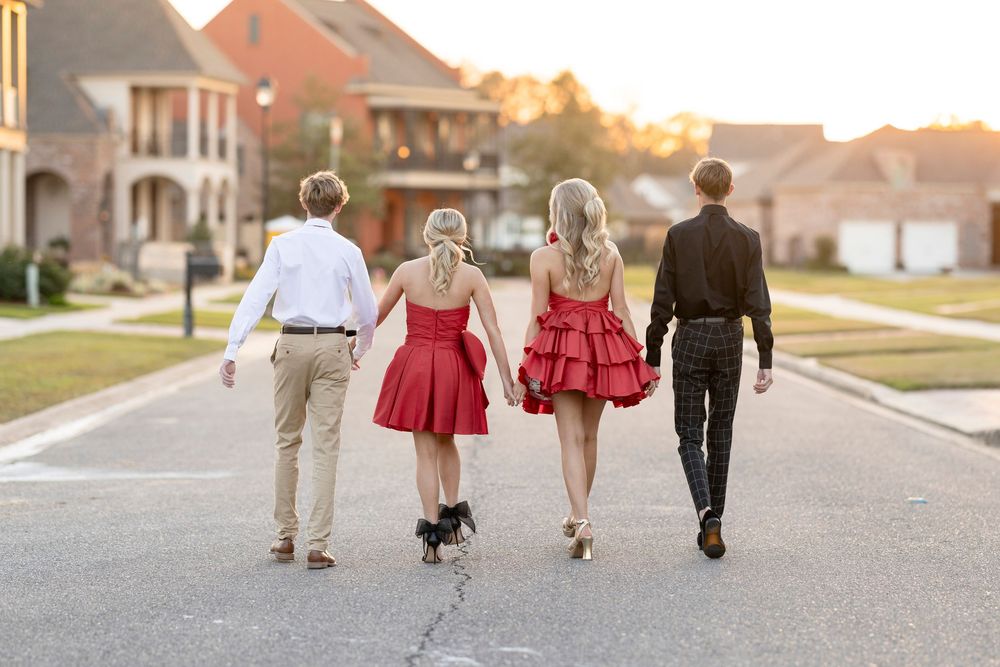 Family in red dresses and casual attire walking away on suburban neighborhood street at sunset.