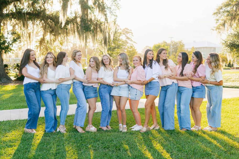 A group of people wearing blue and white outfits poses together on a sunlit grassy lawn.