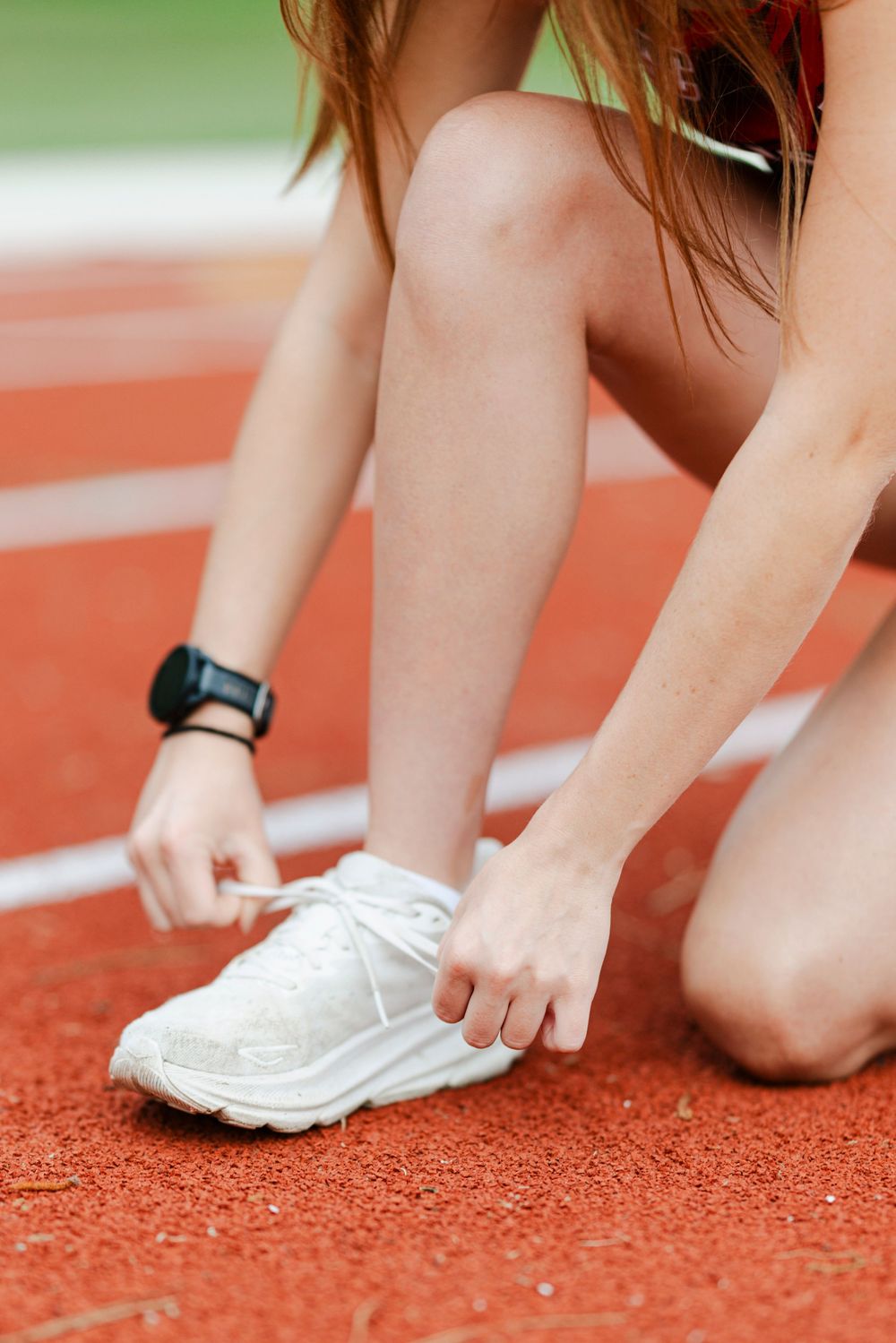 Runner tying white athletic shoelaces on red running track surface.