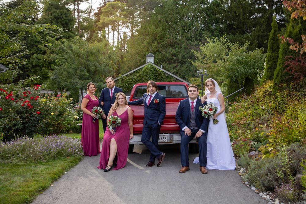 A bridal party staged around a vintage red truck bed in beautiful landscaped garden
