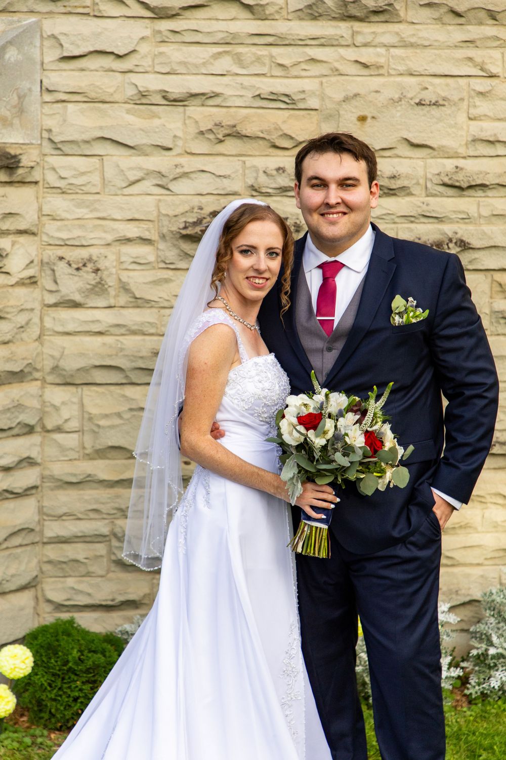 bride and groom smiling at the camera in front of a brick wall