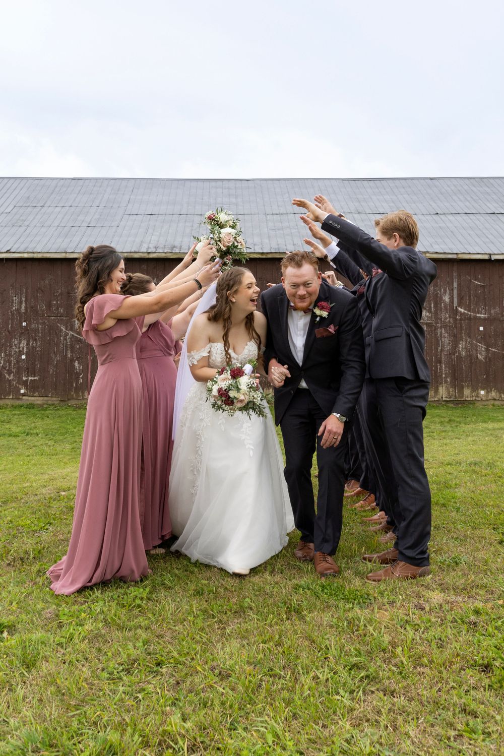 bridesmaids and groomsmen standing in a line while making a tunnel with their arms up in the air for the bride and groom to walk through