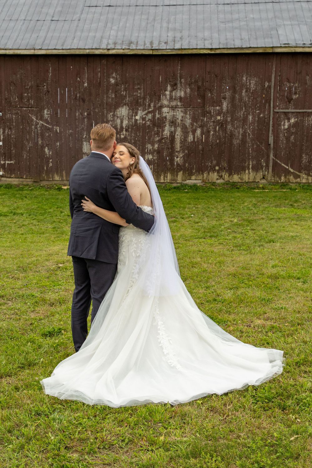 a groom looking away from the camera with his bride hugging his side cuddled into his neck with her dress all fluffed out