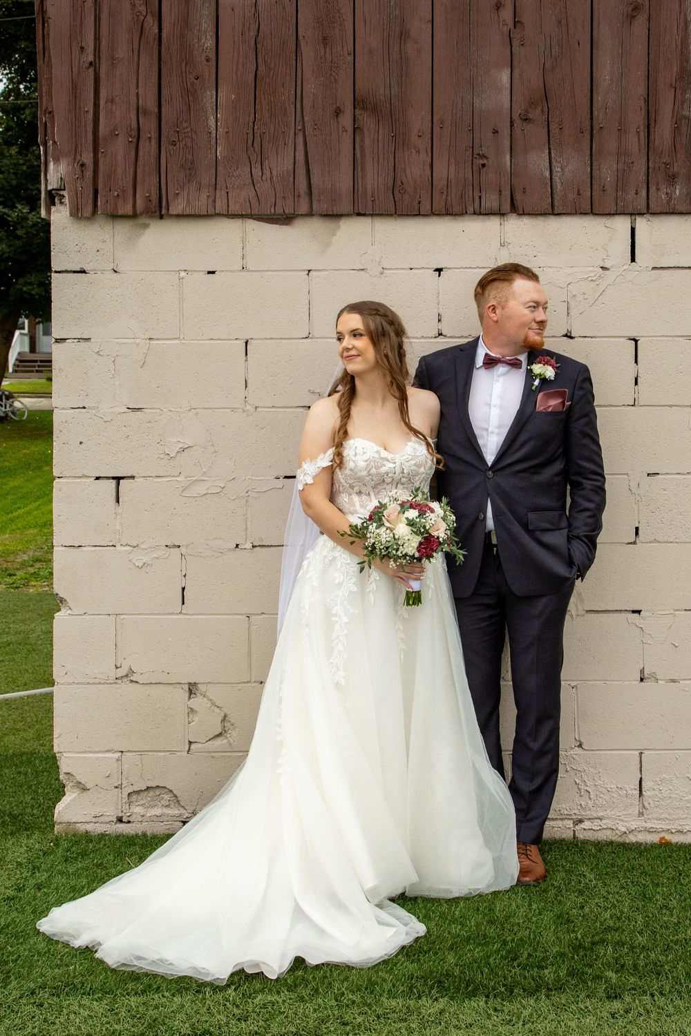 bride and groom smiling at the camera in front of a brick wall looking the opposite directions of each other