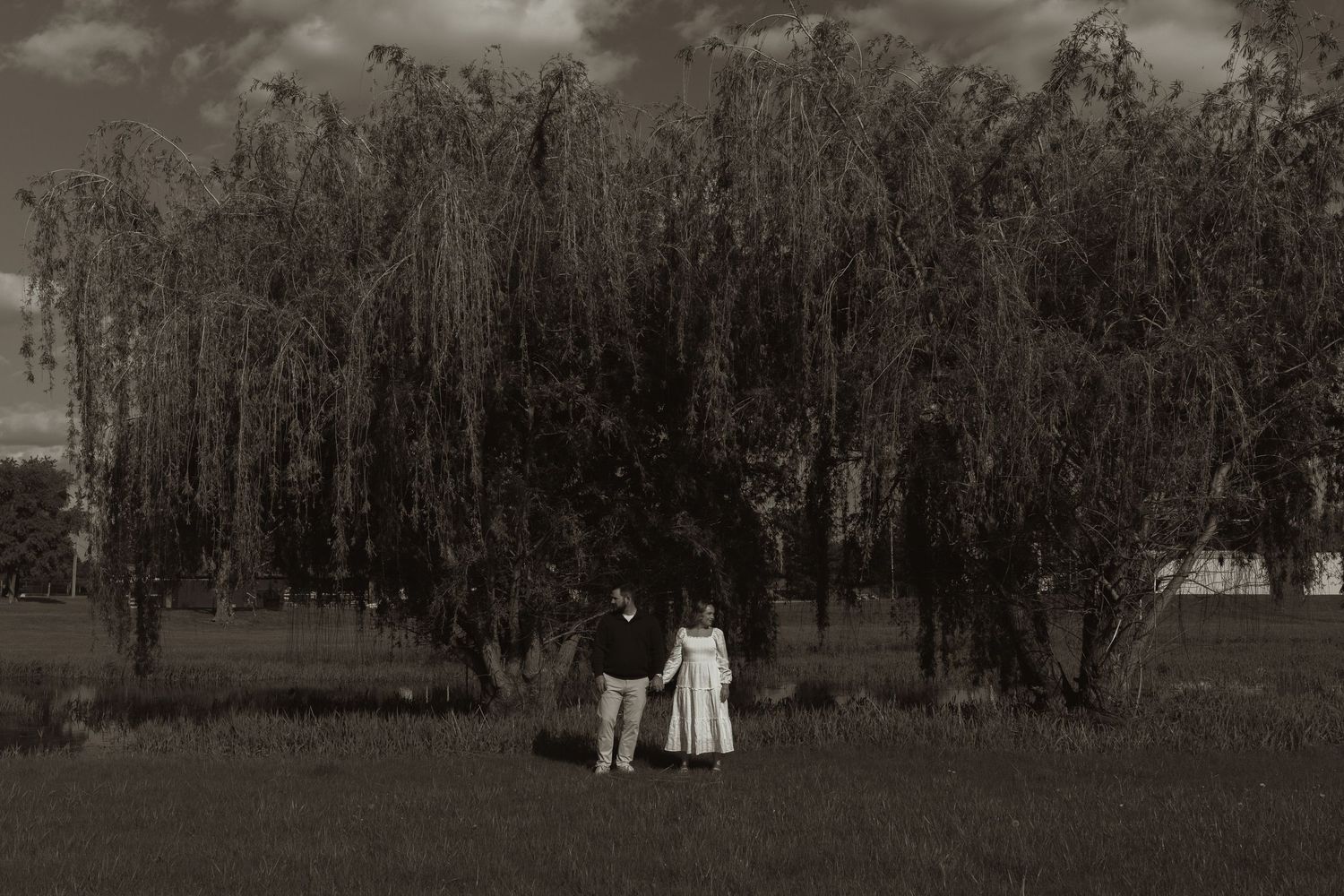 Wedding couple shares intimate moments under large trees in a lush garden setting.