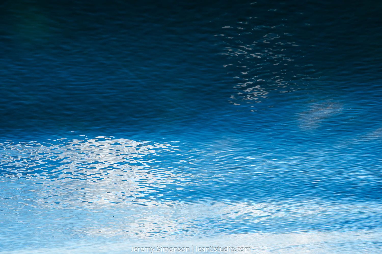 Inverted reflection of cloudy blue sky on calm water surface.