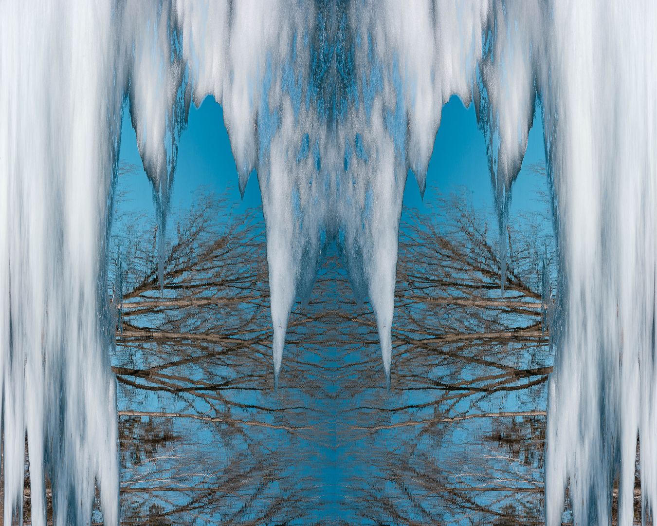 Icy stalactites frame a bright blue winter sky with bare tree branches visible through the frozen formations.
