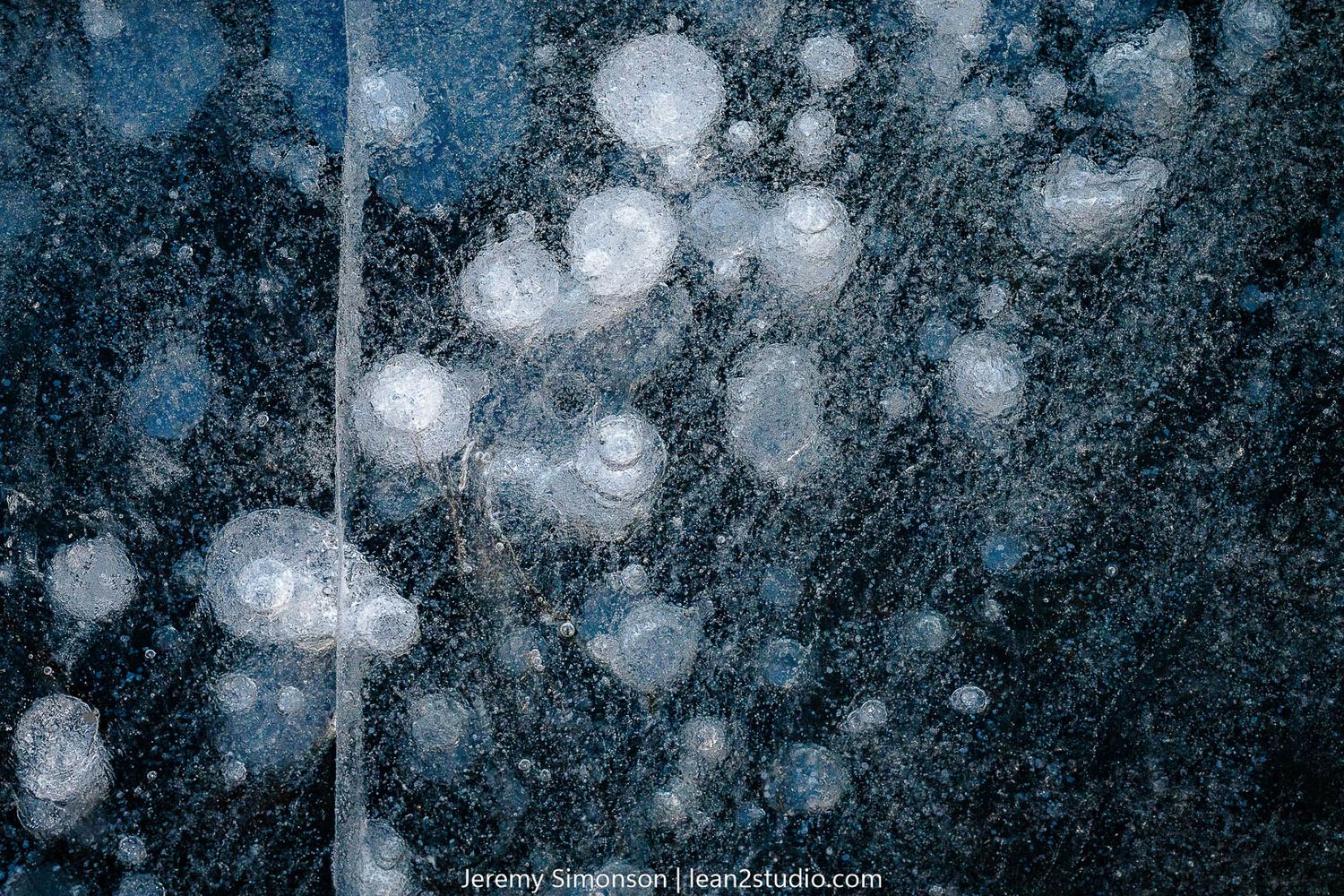 Frozen bubbles trapped beneath ice create ethereal white spots against dark background.
