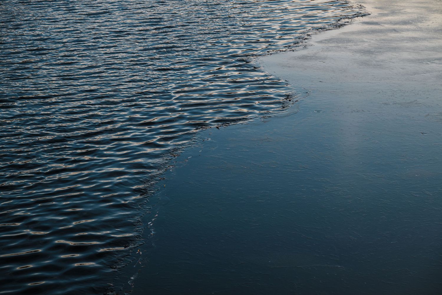 Dark blue rippling water surface with subtle wave patterns reflecting cloudy sky.