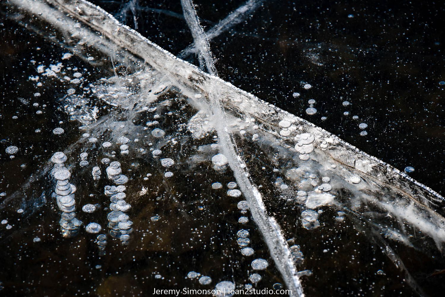 Ice crystals and frozen bubbles form patterns on dark frozen lake surface.