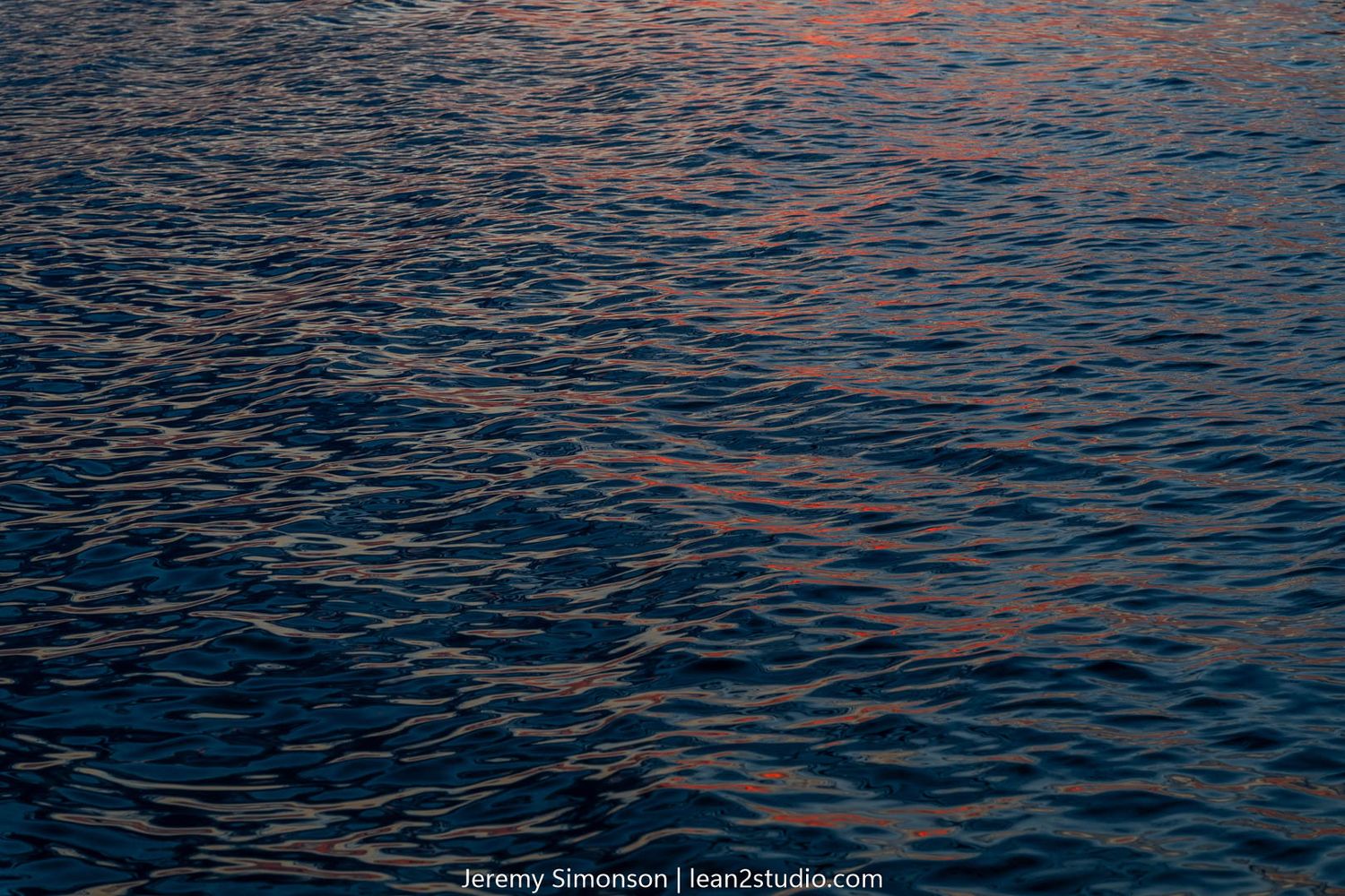 Sunset light reflecting off dark rippling water creating deep blue and orange patterns.