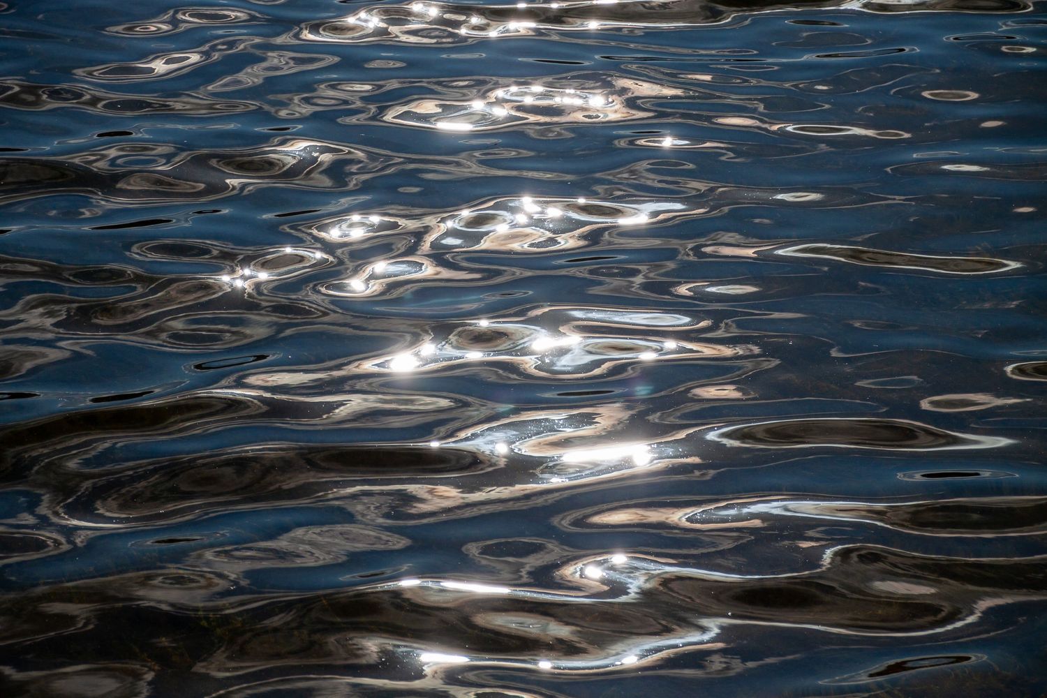 Sunlight reflects off rippling dark blue water creating abstract patterns of light and shadow on the surface.