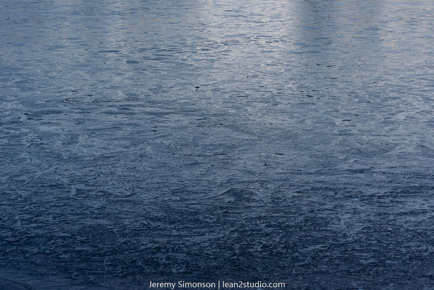 Textured surface of dark blue frozen lake water.