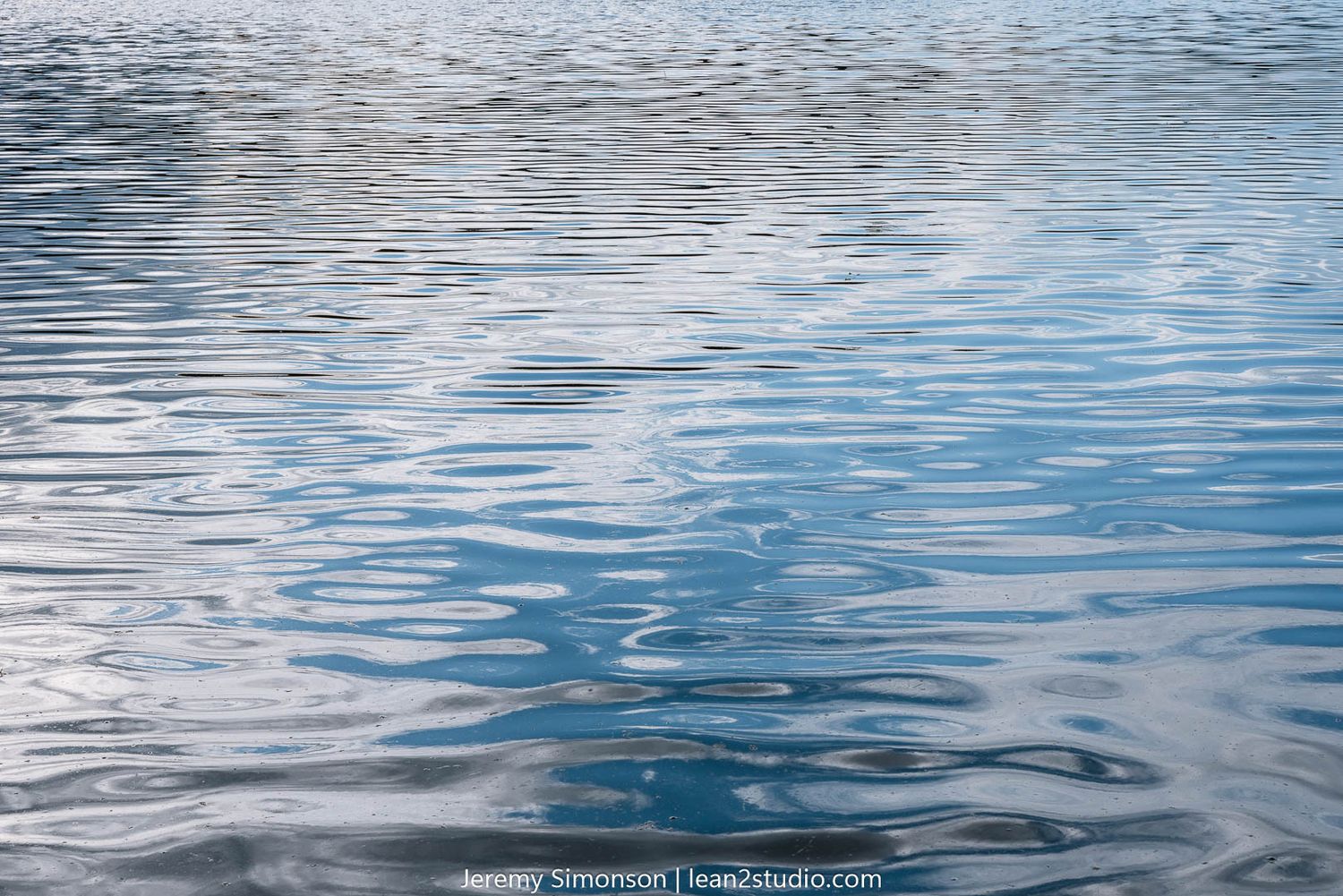 Rippling blue water surface with sunlight reflections creating a serene pattern of waves and movement.