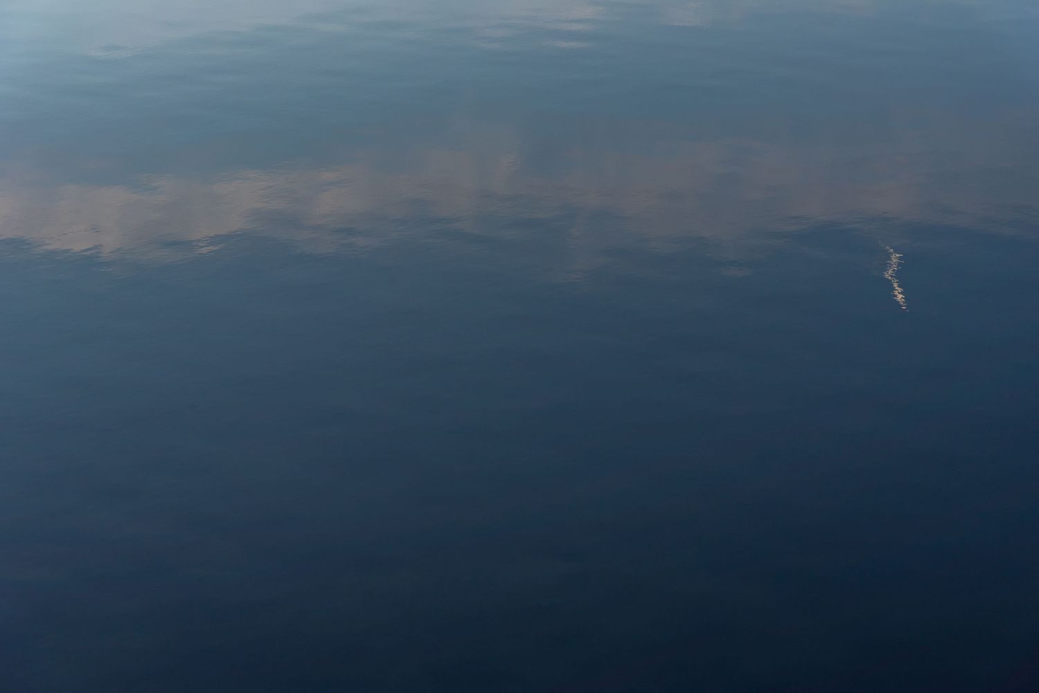 Aerial view of calm blue water surface reflecting clouds in a peaceful seascape.