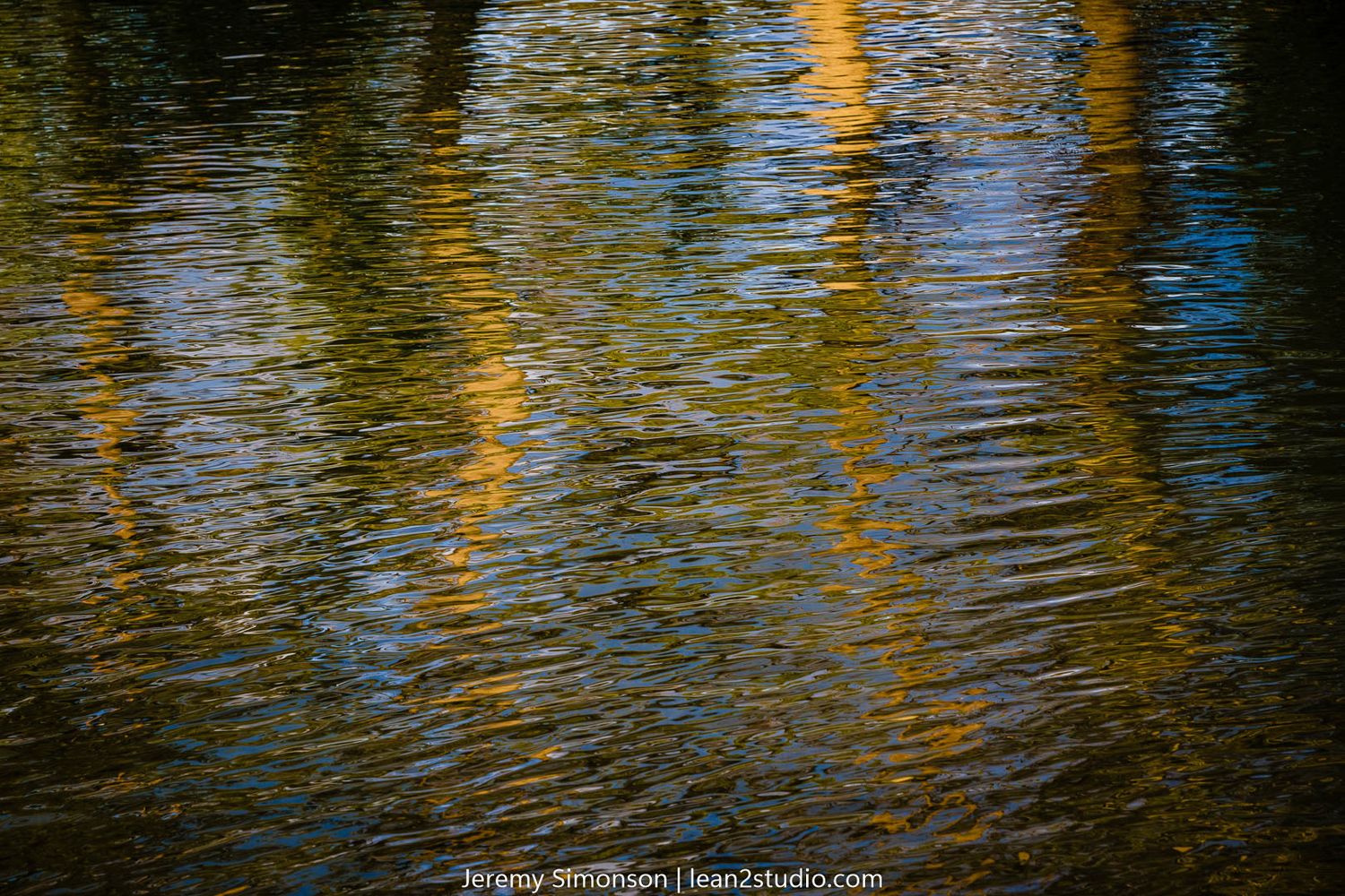 Golden sunlight reflects on rippling water creating abstract patterns of yellow and brown.