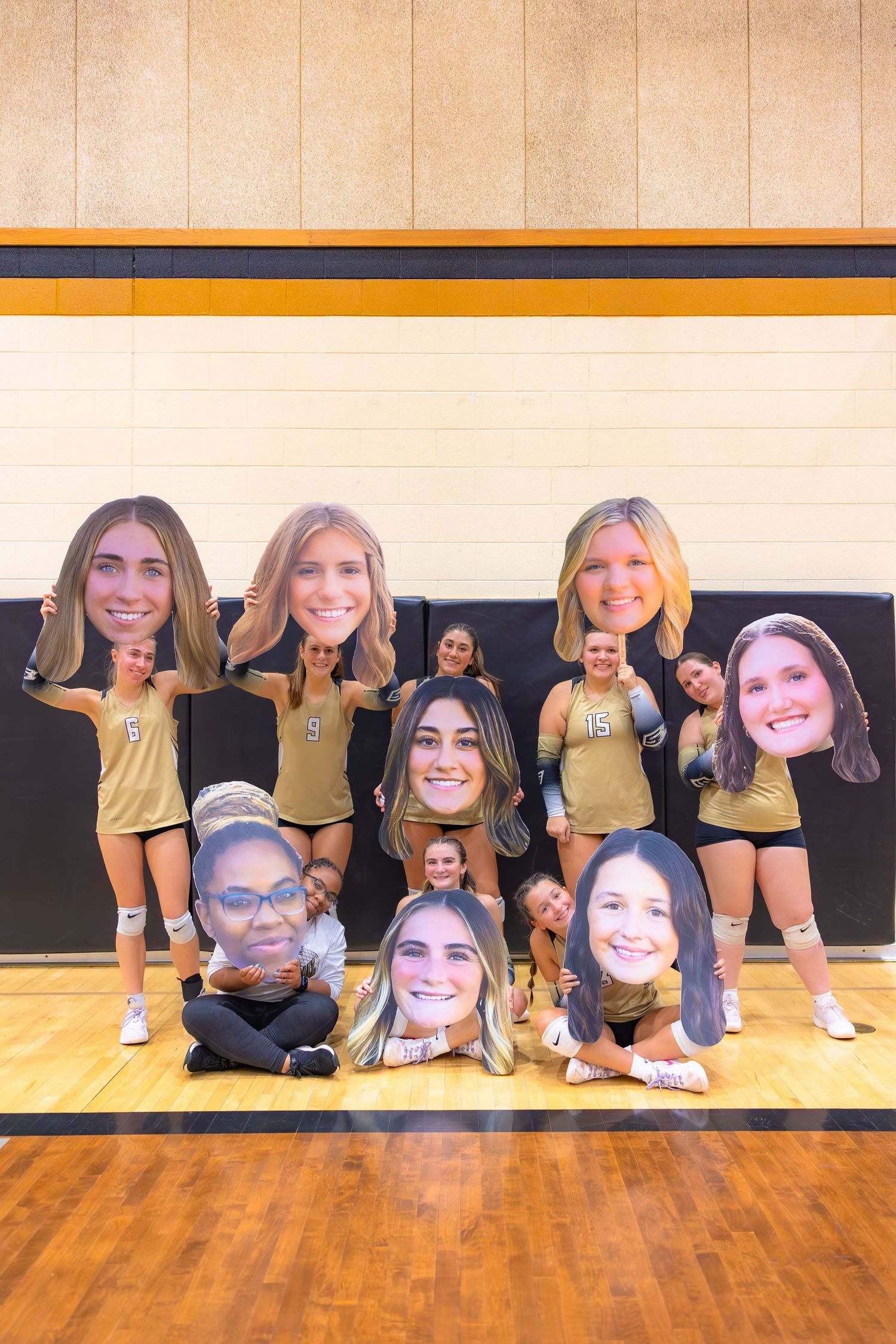 Group of cheerleaders in yellow uniforms pose together on wooden gymnasium floor.