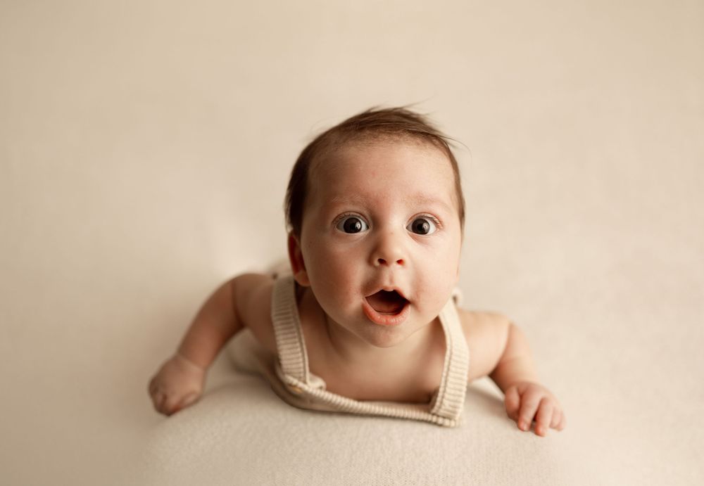 A series of expressive baby photos showing different emotions and poses against a neutral beige background.