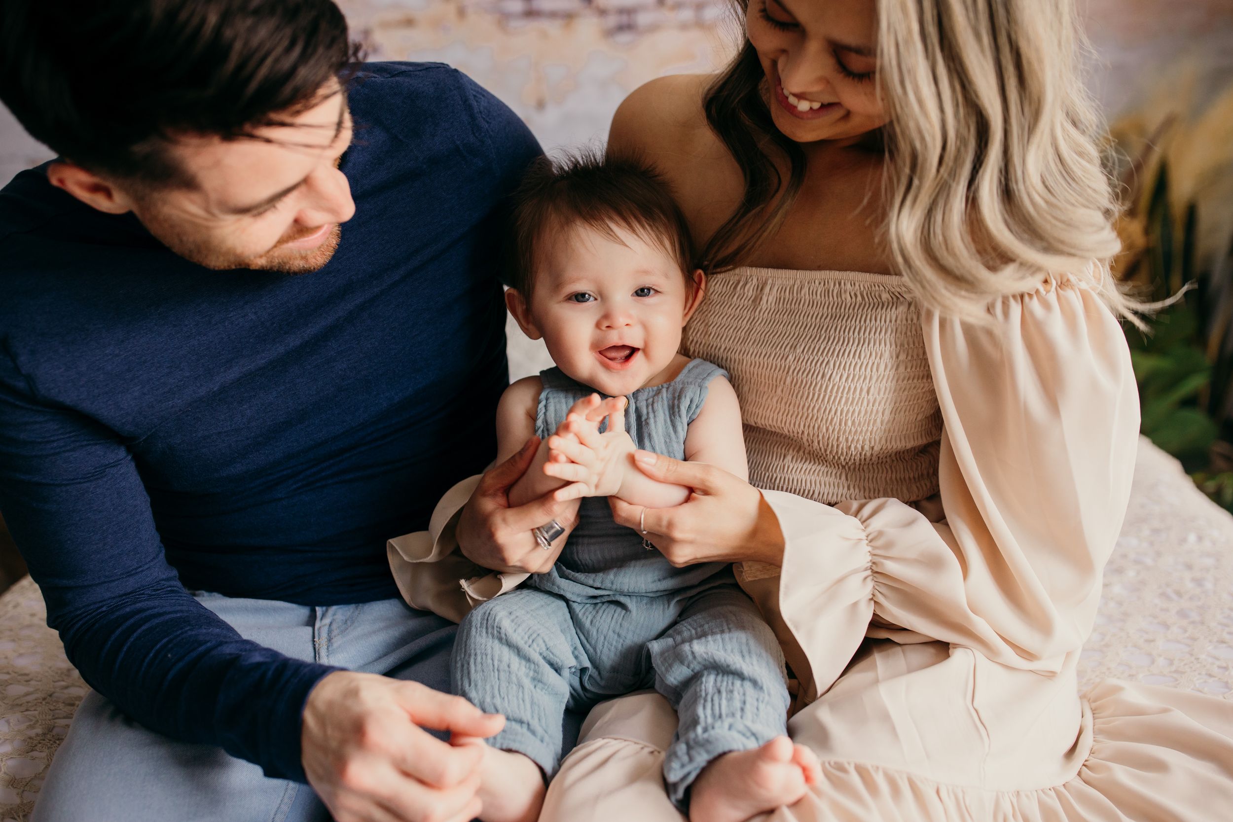 A happy family moment captured on a light-colored couch with parents and their toddler sharing joyful expressions.