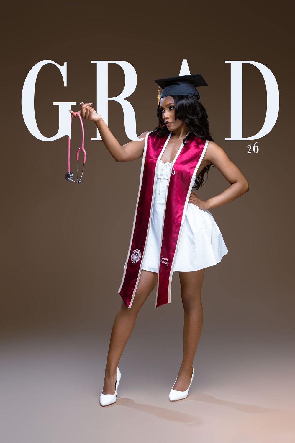 Young woman in graduation cap, white dress, burgundy sash, holding a stethoscope, posing for GRAD 26 photo.