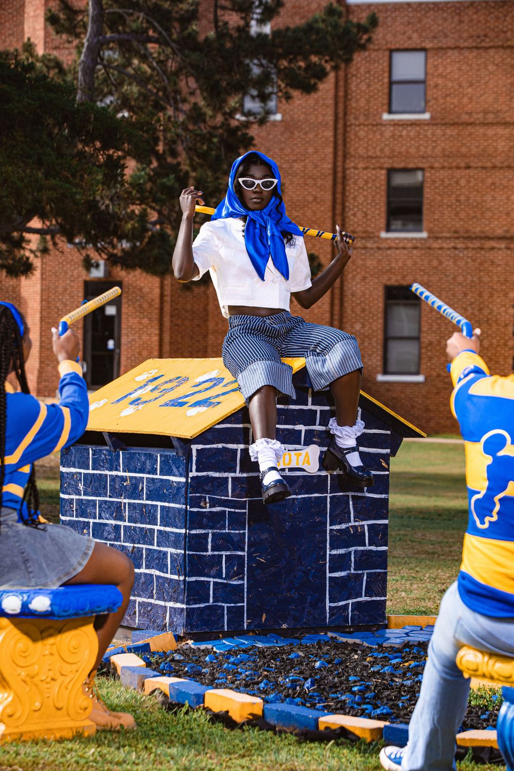 Person in blue headscarf and white top sits on decorative blue brick structure with 1922 sign outdoors.