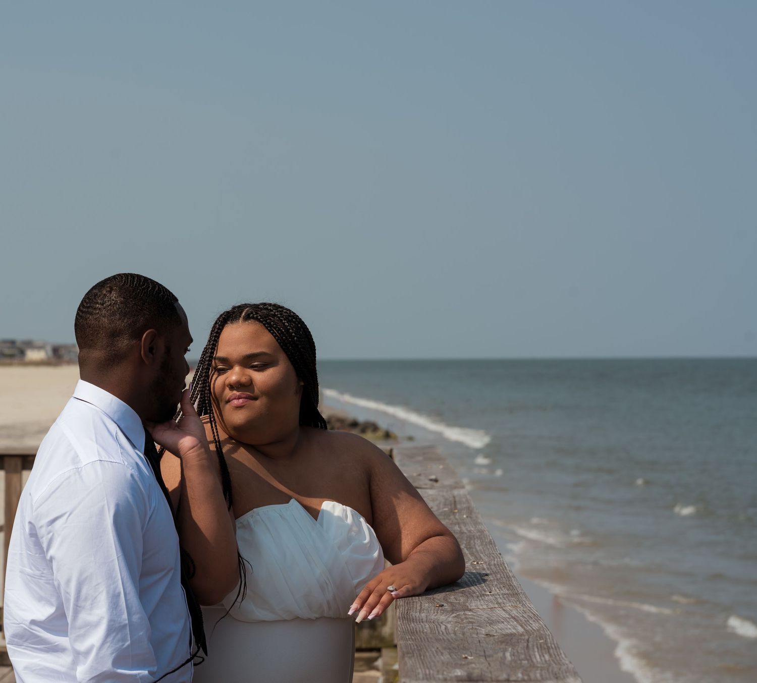 A loving couple embraces and kisses on a beachfront boardwalk with the sea visible in the background.