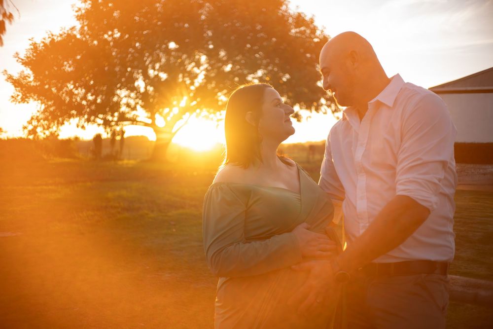 Couple sharing tender moment outdoors with brilliant golden sunset and lens flare behind them.