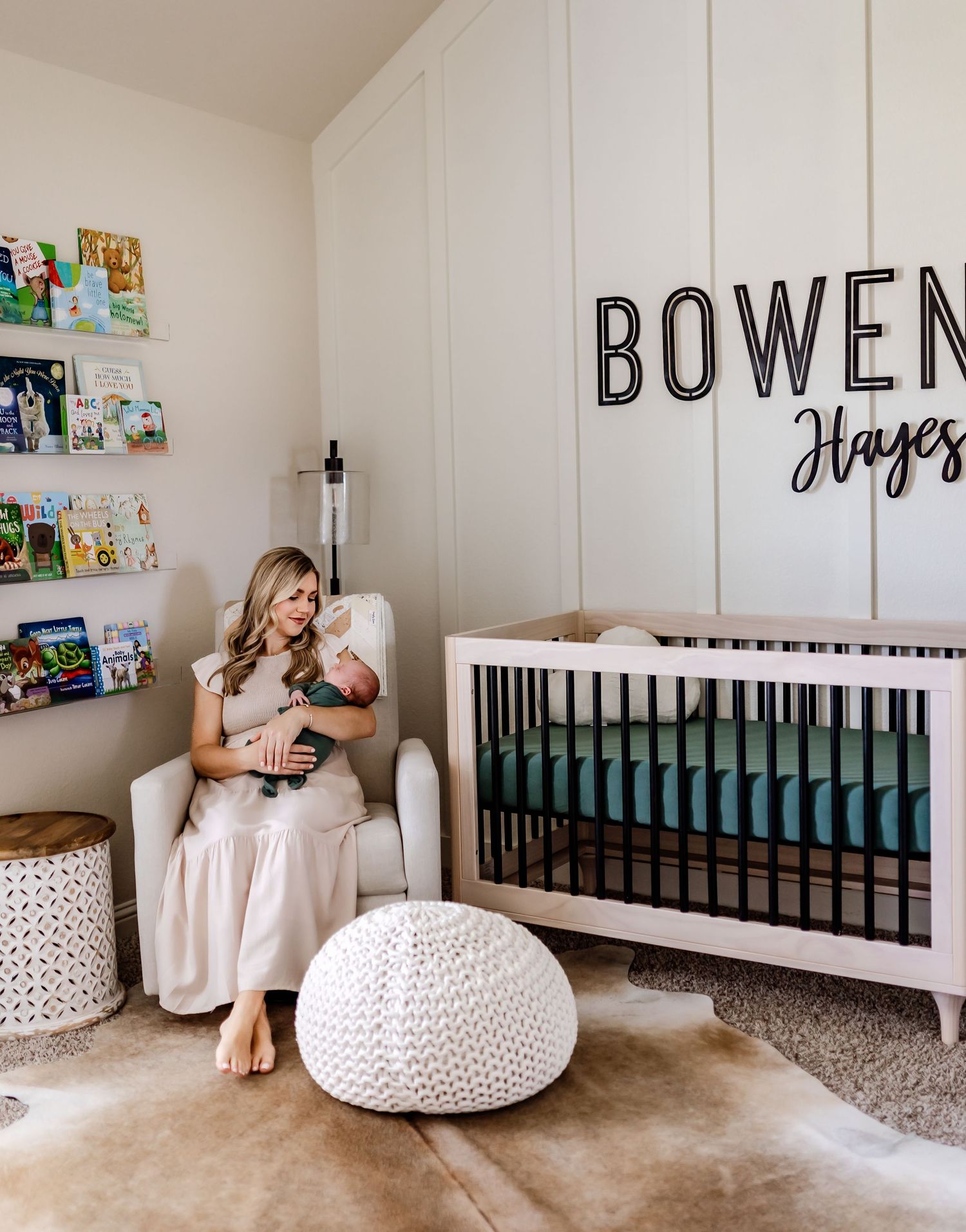 A nursery room with white furniture, displaying the name Bowen and decorative wall shelves.