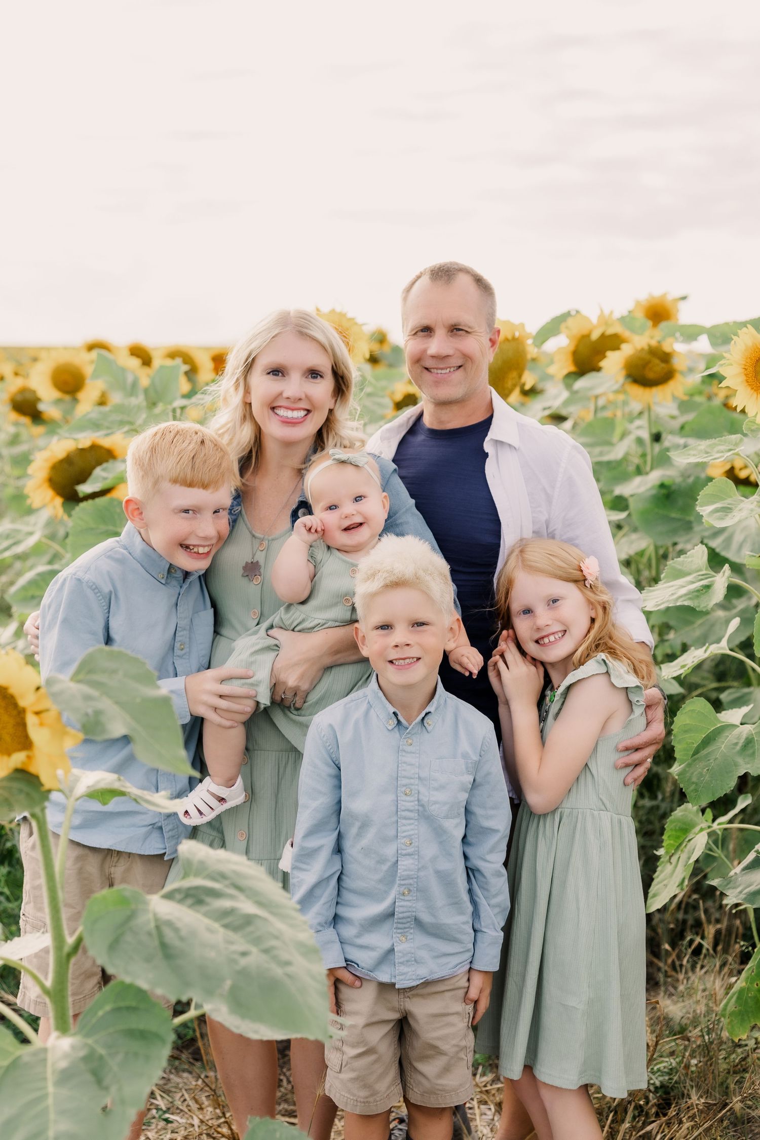 A family group stands together outdoors among evergreen trees at sunset wearing coordinated casual attire.