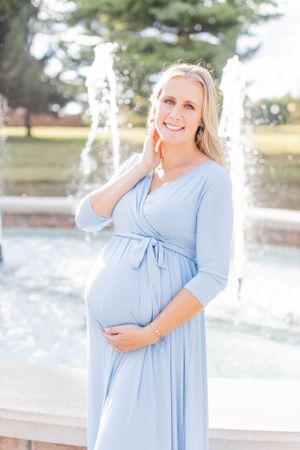 Expectant mother in light blue dress poses by outdoor fountain in Springfield, Missouri.
