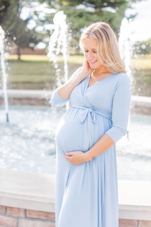 Expectant mother in flowing blue dress poses by fountain in Springfield, Missouri.