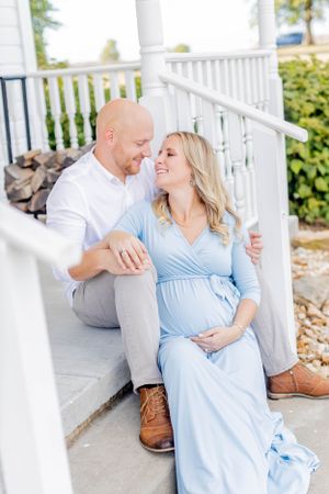 Couple shares tender moment on white porch during maternity photoshoot in Springfield, Missouri.